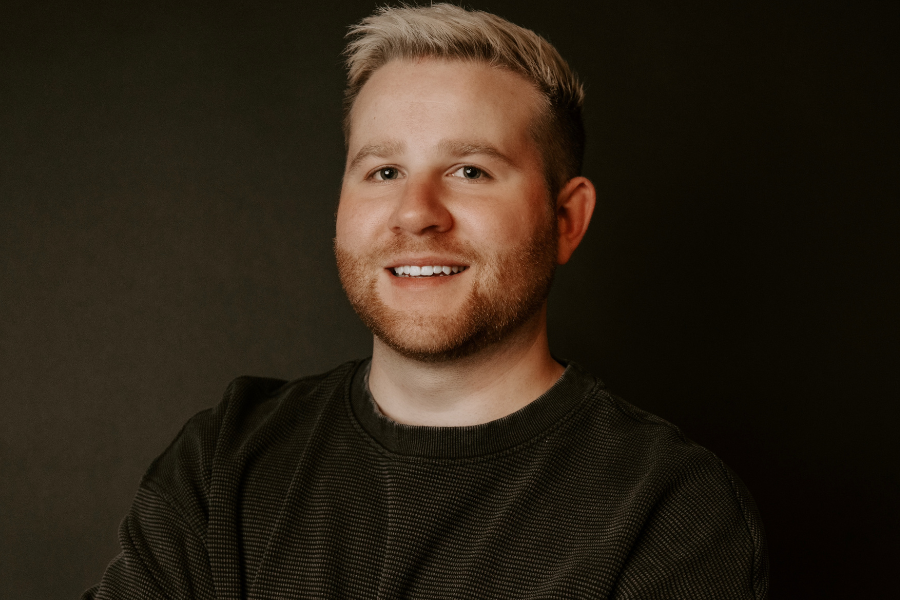 KSU alumnus Bryan Webb smiling with his arms crossed in front of a black background