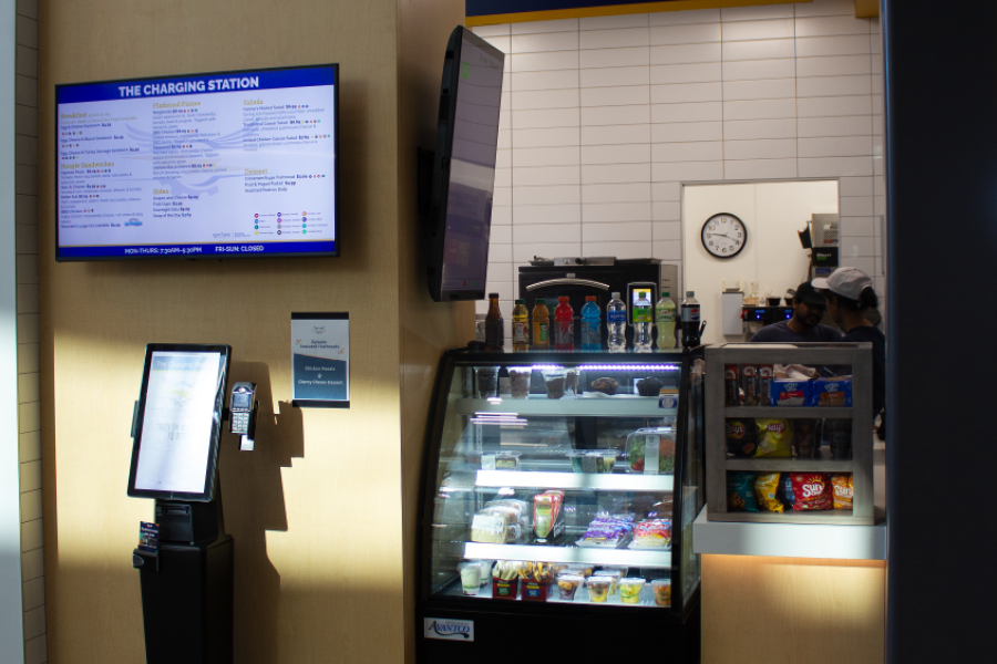Front view of the Charging Station, displaying a Menu Screen, an ordering kiosk, and a display case with food and drink items
