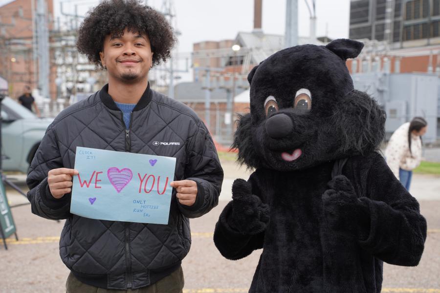 Man with "we love you" sign posing with black squirrel mascot