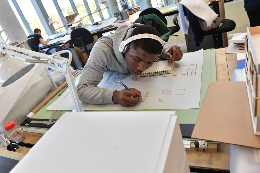 A student carefully draws on a large piece of paper in a studio.