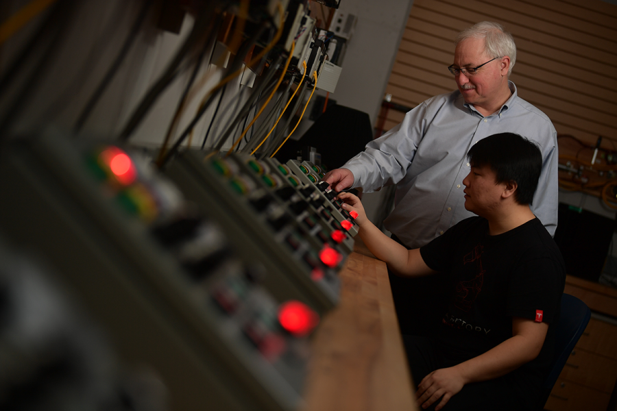 A teacher guides a student in using a machine.