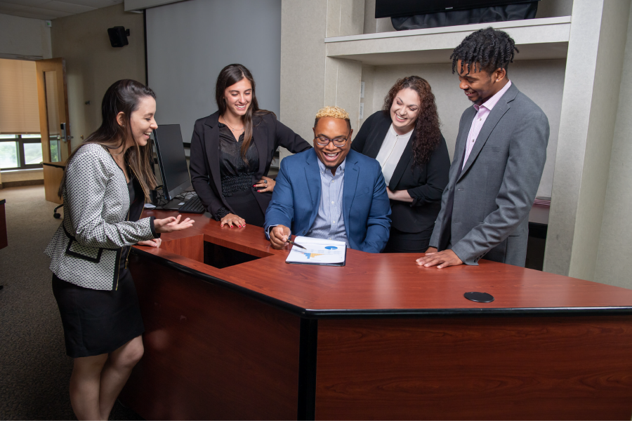 A group of students gather around a table, wearing formal attire, and smiling. 