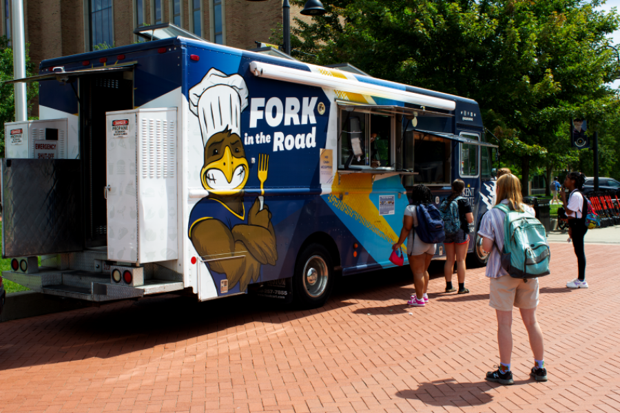 Four students standing near the Fork in the Road Food Truck parked on the Risman Plaza