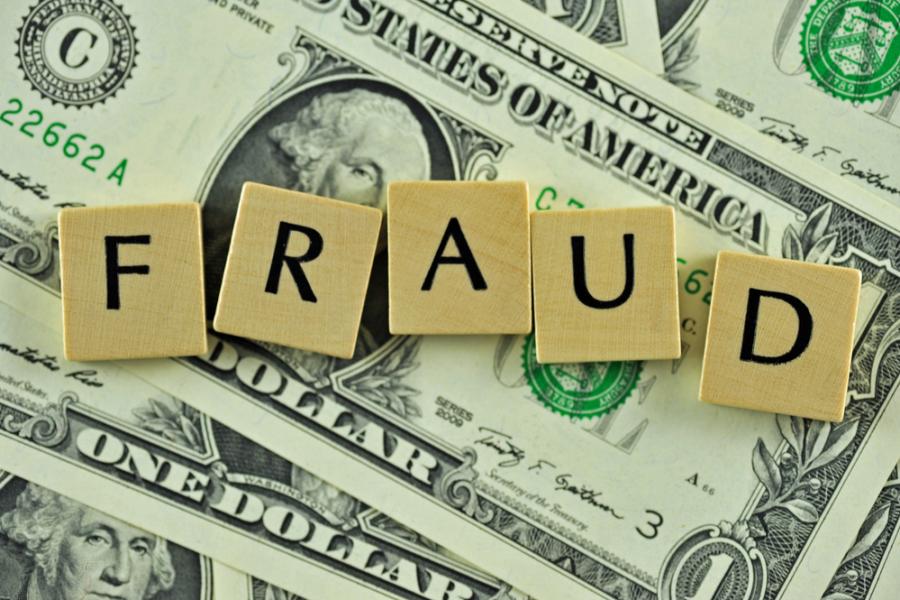 Scrabble tiles spelling "fraud" sitting on top of a pile of dollar bills.