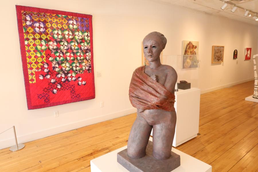 Sculpture in the center of an art gallery with artwork hanging on the wall behind