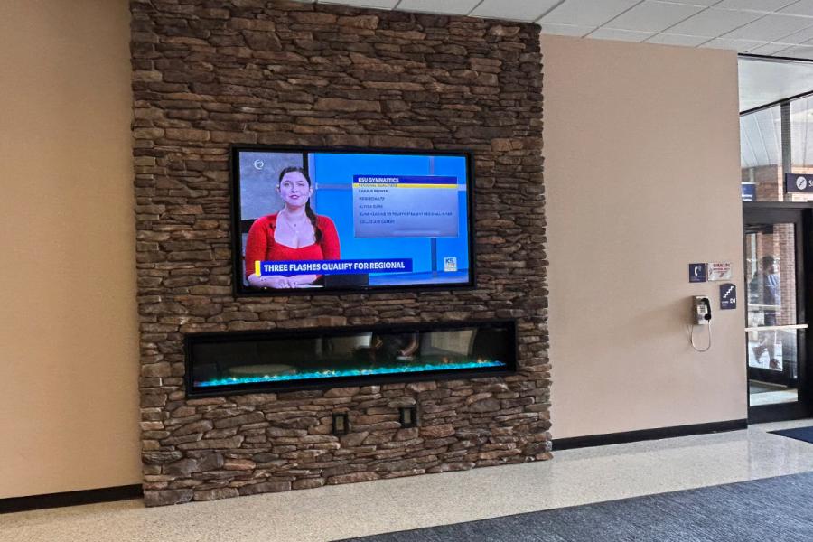 Large screen above fireplace in student center with KSTV news showing on it