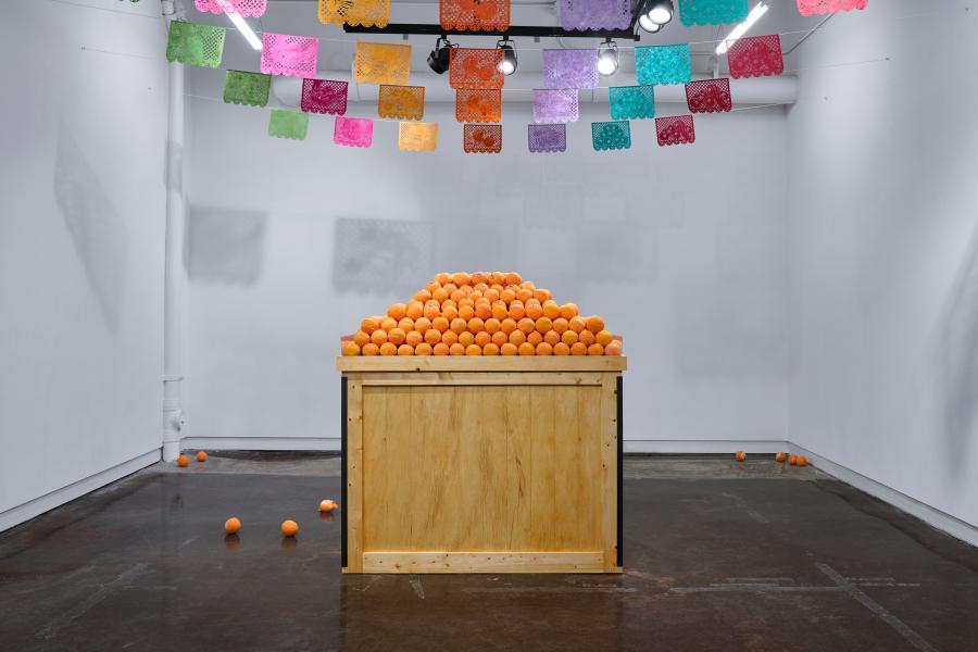 a sculpture replicating the look on an orange stand, but the oranges are moldy. Above colorful paper bunting adorns the ceiling