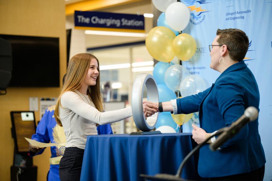 An engineering student extends her right hand through the Order of the Engineer ring sculpture while participating in the induction ceremony at Kent State University.
