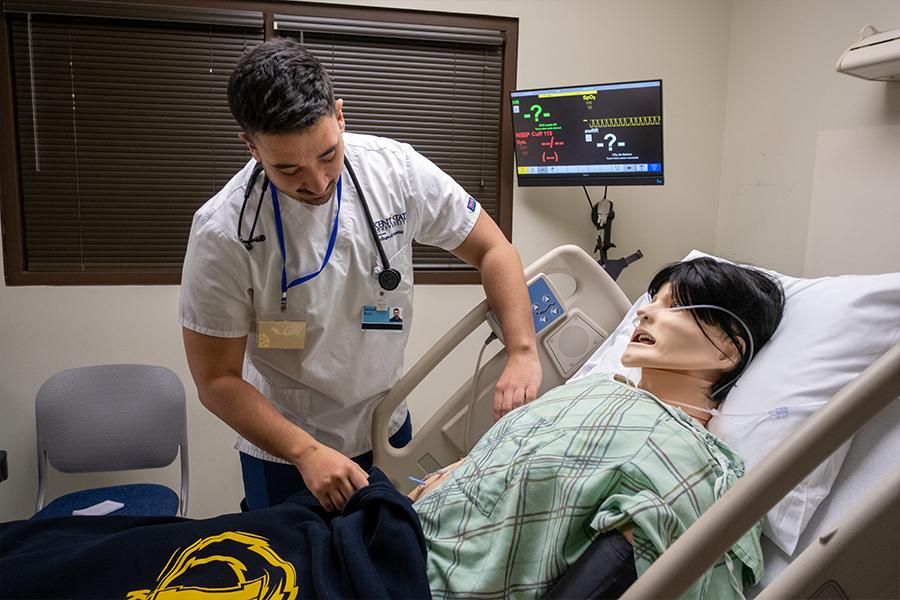 Male nursing student practicing in the simulation lab on a nursing manikin.