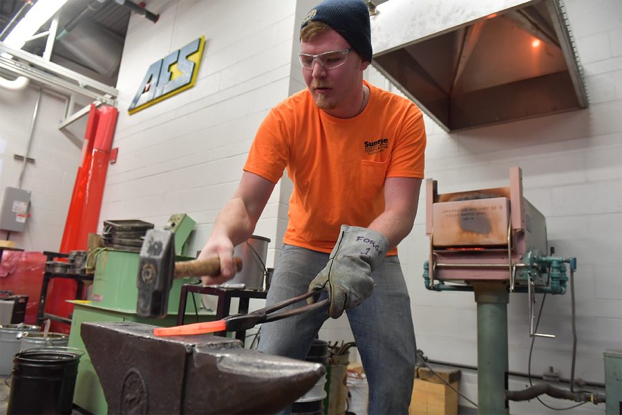 A student smiths a piece of metal on an anvil.