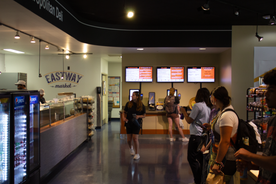 Students waiting for their food orders in front of the counter at the Metro Deli in Eastway, menu screens and order kiosks visible in the background