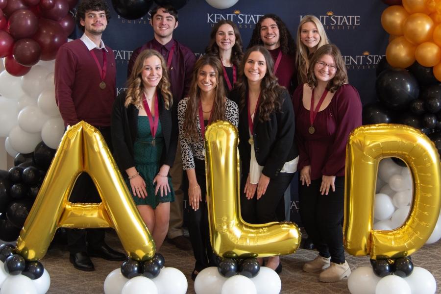 lpha Lambda Delta leadership board members pose underneath a red, black, gold and white balloon arch with gold balloons in front of them spelling out “ALD”.