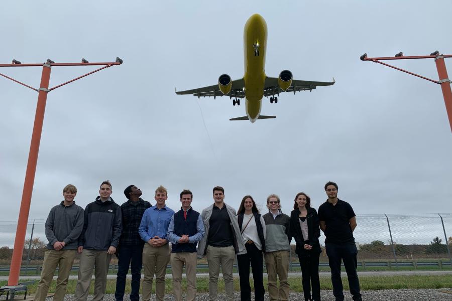 Philip standing with fellow aeronautics students at the airport with a plane flying above