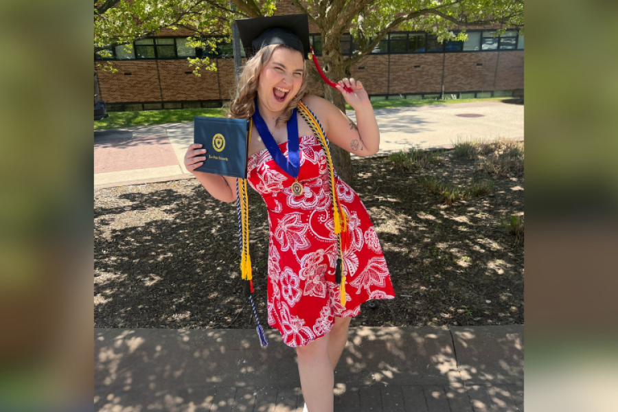 KSU Alumna stands in front of brick building with Graduation cap on and diploma in hand, smiling