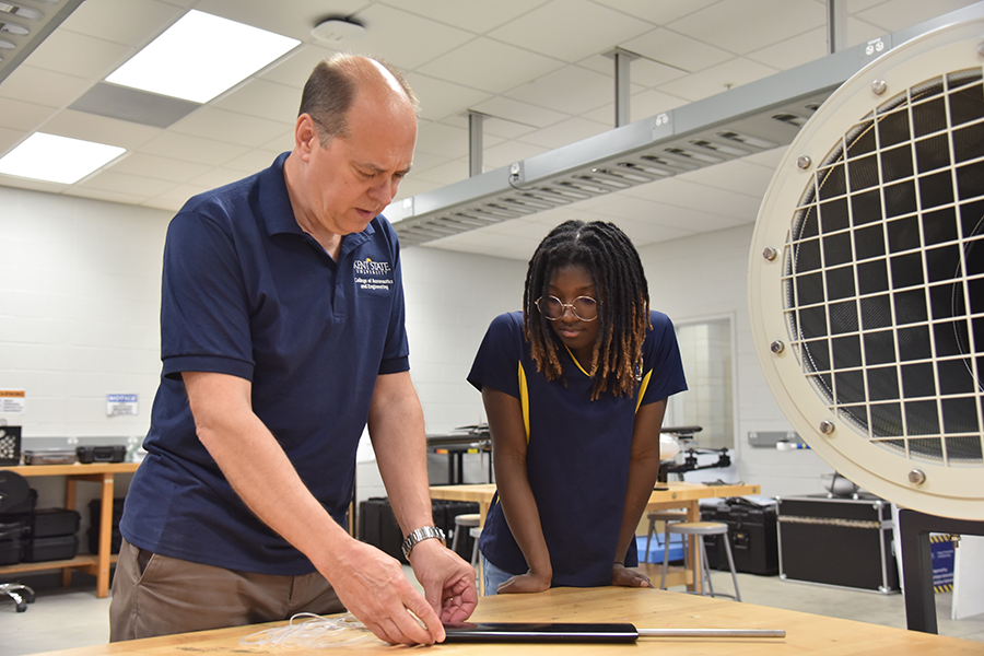 An older white man in a blue shirt helps a student fit an aerofoil with probes for use in an experimental wind tunnel