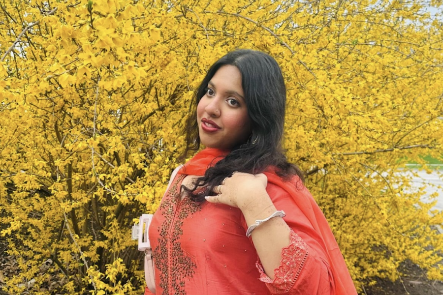 Ittiba in a red dress next to a yellow flowering bush.