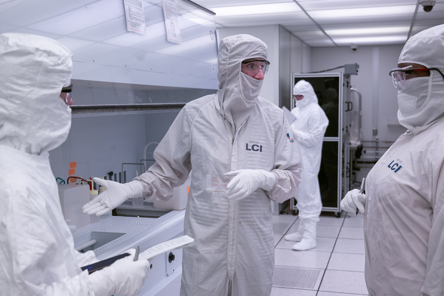 Three people talking in a cleanroom.