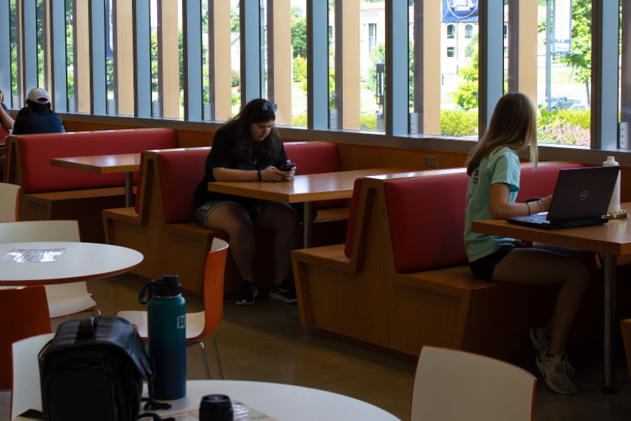The seating area at the Simon Café, consisting of booths and individual tables. A student's belongings are sitting at one of the tables and there are students sitting at some of the booths