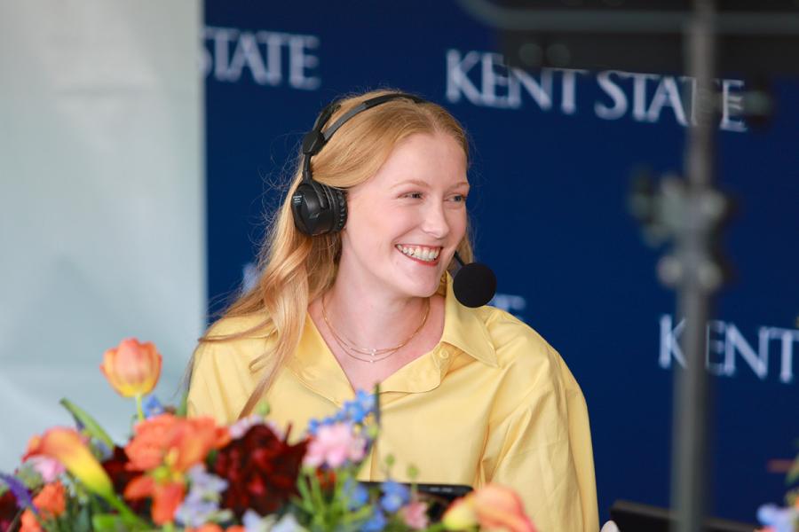Student Sydney Brown poses with flowers while wearing a broadcast headset