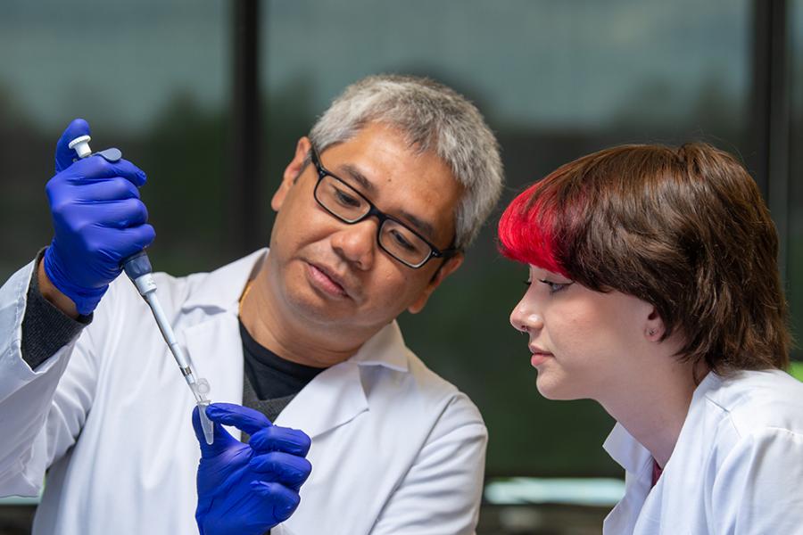 A photo of a younger student with split-dyed hair observing an older faculty member.