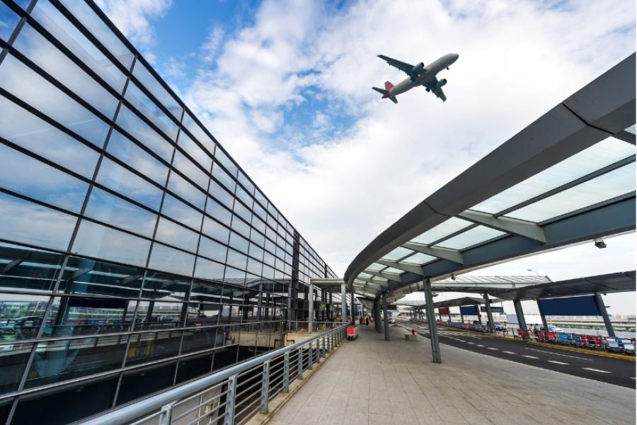Photo of airport with plane flying in sky above.