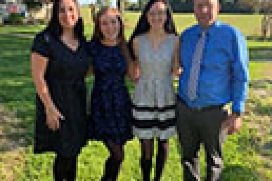 Photo of Angie ang Gregg, posed with their two daughters, on a sunny