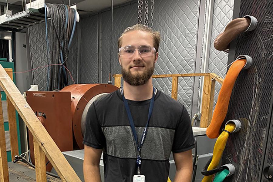 A young man wearing a dark t-shirt and jeans in a workroom