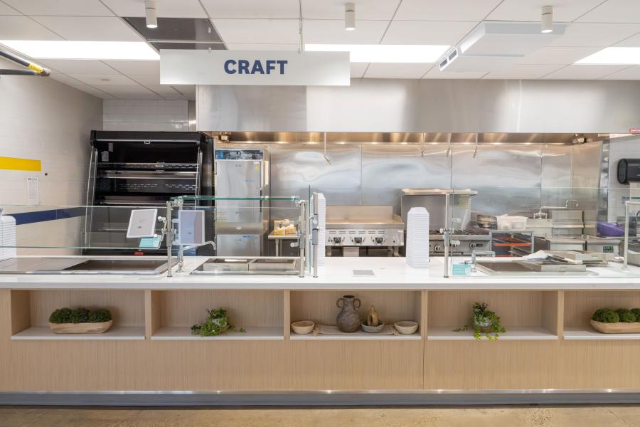 Front view of DI Dining "Craft" station, featuring prep counters, fryers, a stove, and stacked plates