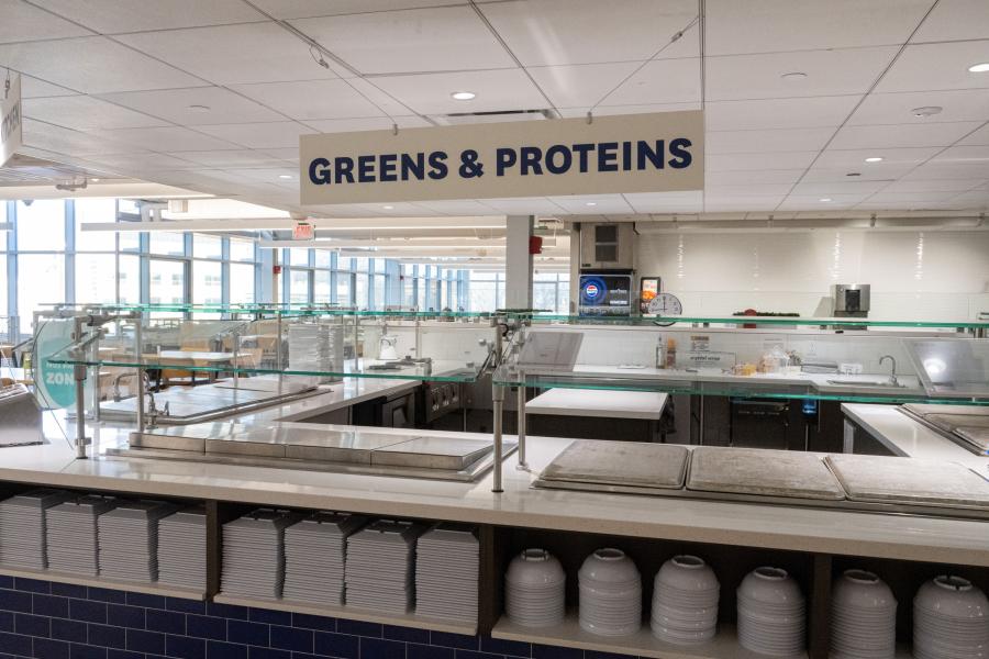 View of Di Dining's "Greens & Proteins" area, featuring prep counters and stacks of plates and bowls