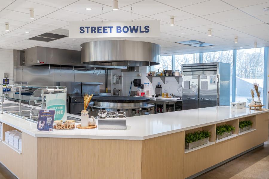 View of DI Dining's "Street Bowls" area, including prep counters and a kitchen area with a large, circular flat-top grill in the center