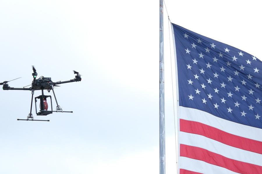 A quadcopter drone carrying a football in front of an American flag