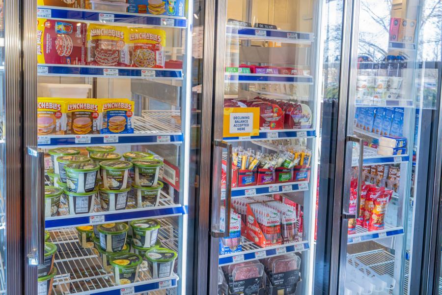 Close up of a display cooler in Eastway Market, featuring products like various cheeses, Lunchables, and yogurt