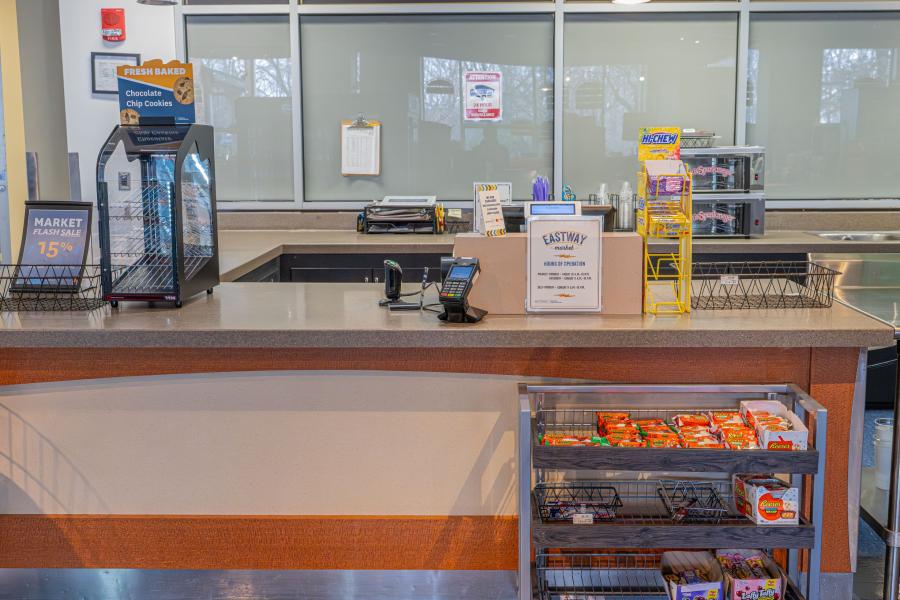 Front view of the checkout counter at Eastway Market, including a register, payment device, and a small display shelf with candy