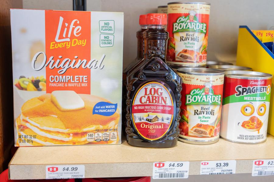 Close up of a shelf with products at Eastway Market, including pancake mix, syrup, canned ravioli, and canned Spaghettios