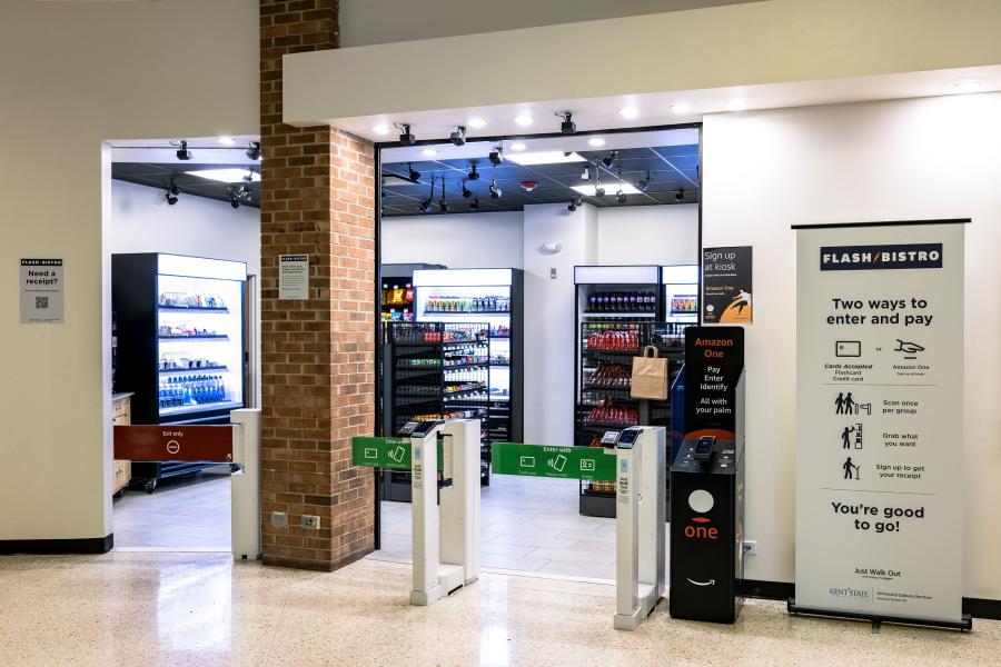 Entrance to the Flash Bistro, featuring a sign-up kiosk, two payment lanes with payment devices attached, and food/beverage display cases visible inside