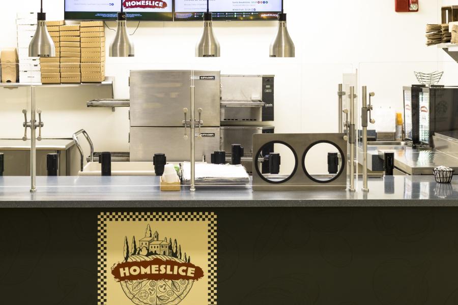 Front view of the Homeslice counter and food prep area, with the main oven visible in the background