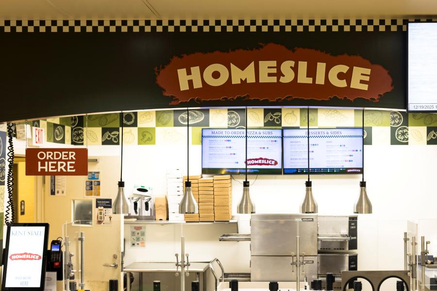 Front view of the Homeslice exterior, including the Homeslice logo above the counter with menu screens visible on the back wall