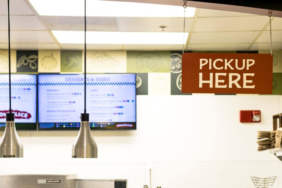 Close up of Homeslice's pick up station, which a red sign hanging from the ceiling that reads "Pick Up Here"