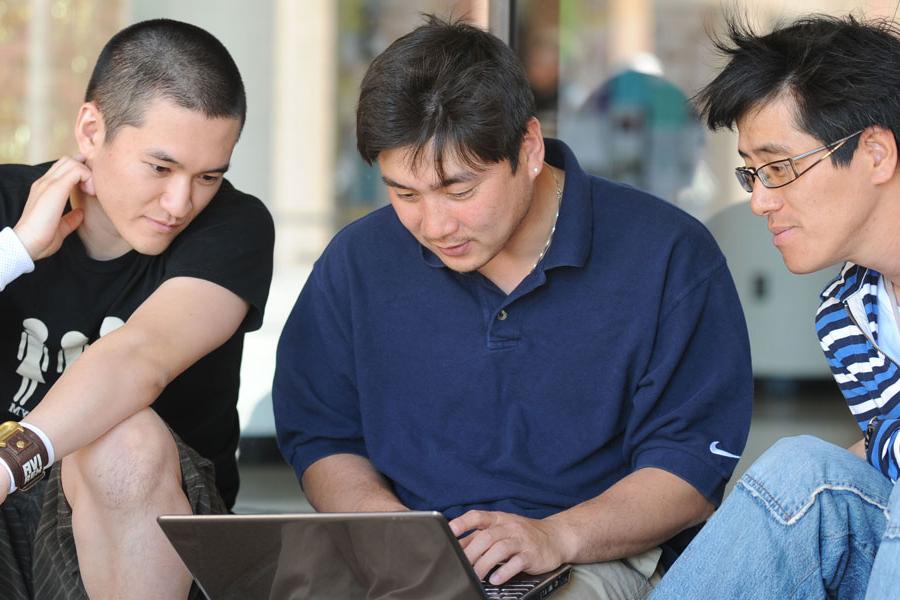 Three students sit around a laptop in the University Library.