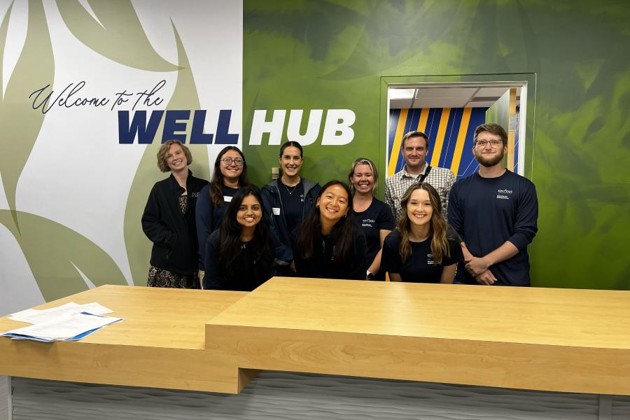 Well Hub staff smiling and standing in front of the entrance to the Well Hub room
