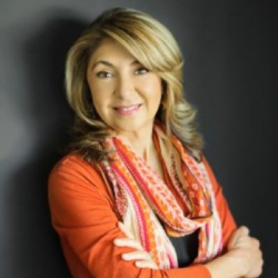 Faculty Member Dr Bonnie Shaker smiling at the camera with an orange blouse