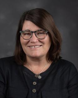 Head-and-shoulders professional headshot of a woman with a studio background.