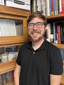 Man with shirt and glasses books in background