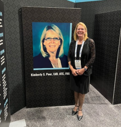 Dr. Kimberly Peer standing next to a display with her photo and information at the National Athletic Trainers' Association Hall of Fame award ceremony.
