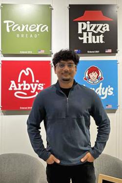 A young man wearing a blue sweater standing in front of several restaurant logos.