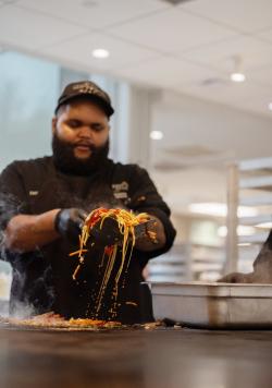 A chef in sautees noodles and scoops them. 