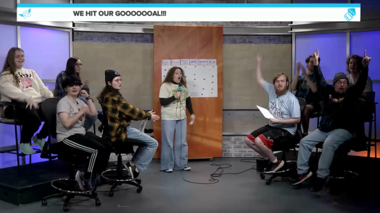 Kent State student media team cheers on a studio set as a host with a microphone announces they hit their fundraising goal during a live broadcast.