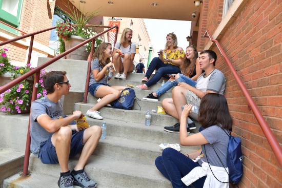 A group of students sitting outside on concrete stairs, talking and smiling