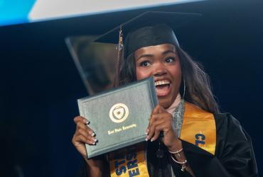 A new 91㽶Ƶ University graduate smiles as she holds her diploma during her commencement ceremony. (Photo credit: Bob Christy, 91㽶Ƶ University)