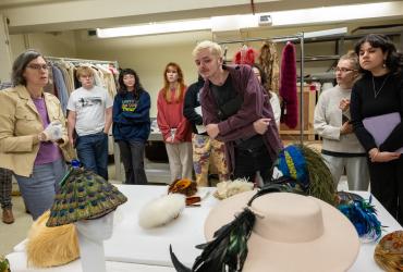 Group of students gathered around a table looking at feathered hats